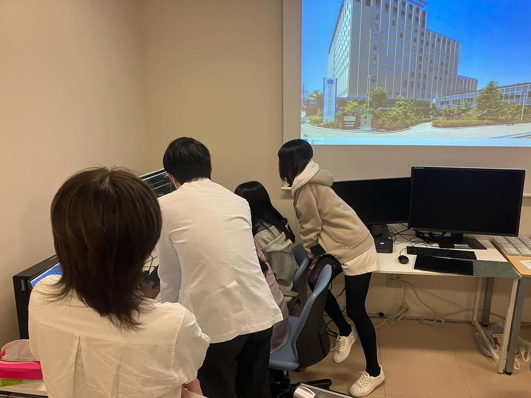 パソコンの並ぶ部屋で、施設紹介のスライドを見る参加者たち